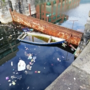 old half sunken row boat surrounded by rubbish in a canal